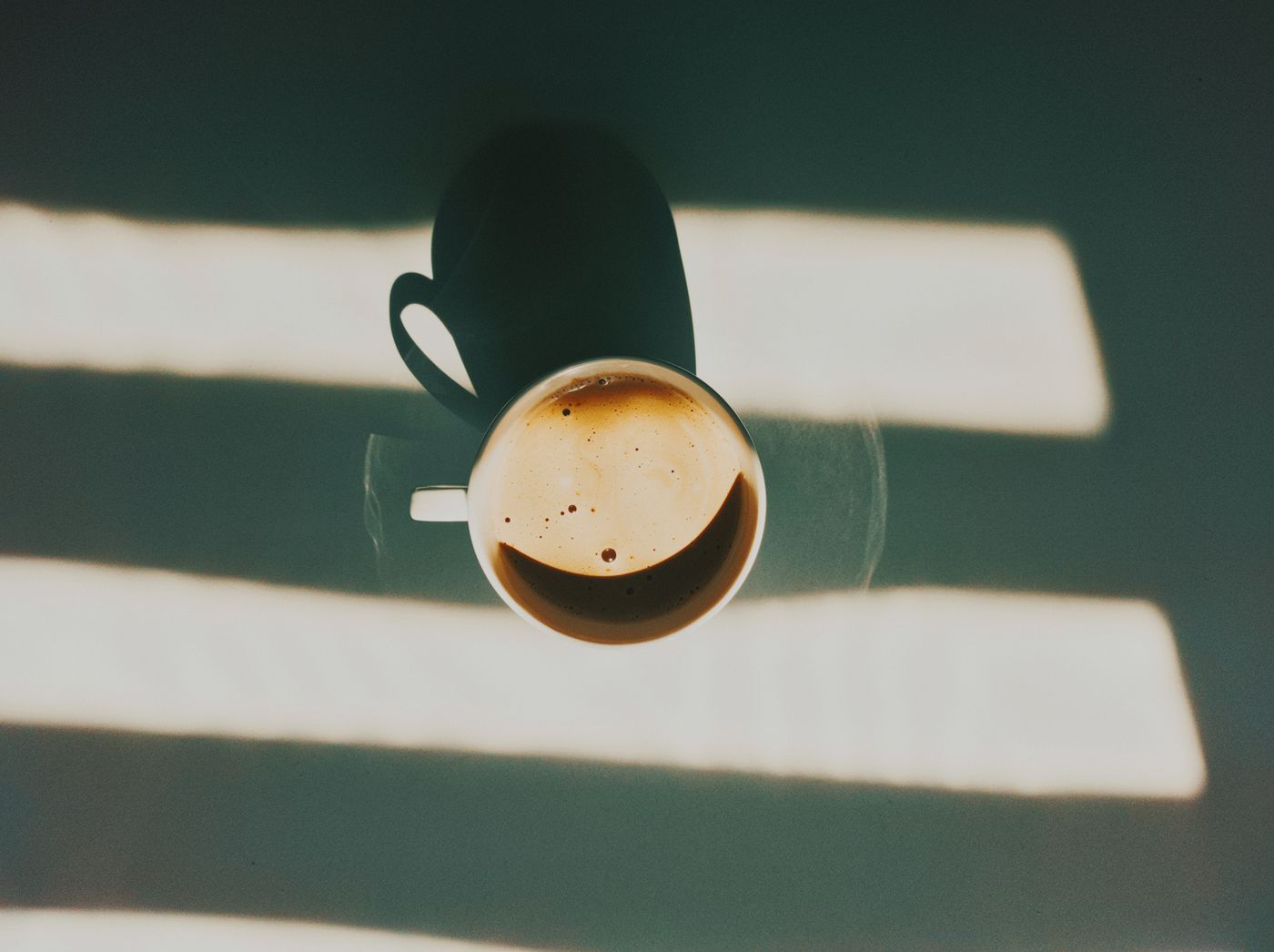 Espresso van bovenaf, met strepen schaduw over het tafelblad.